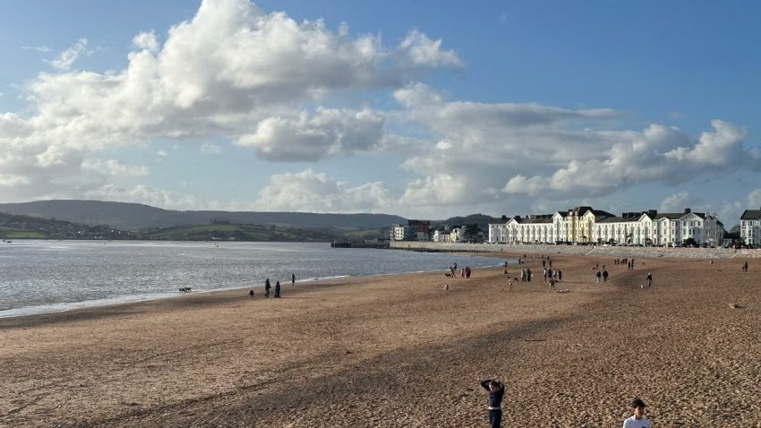Serene beach scene with people and coastal town under blue sky.