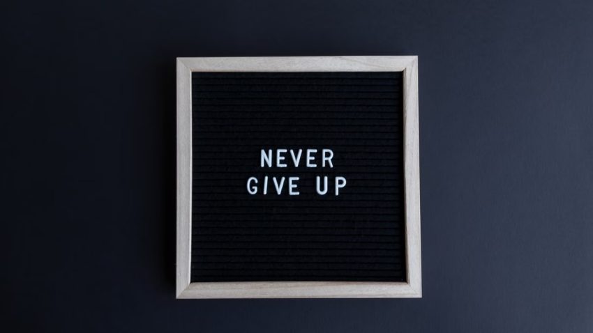 Inspirational letter board with 'Never Give Up' phrase on gray background.